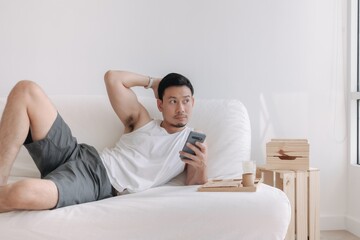 Asian man using mobile phone on his sofa in a relax day off at home. High quality photo