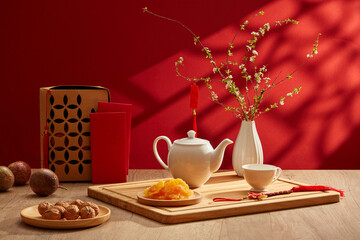 A tea set placed on wooden tray with dried candy and flower pot. Red-themed background for new year...