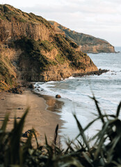 A New Zealand beach and the rugged coastline cliffs at sunset.