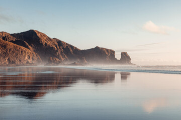 Piha beach captured at sunset, with the warm colors of the sky reflecting on the tranquil ocean waves.