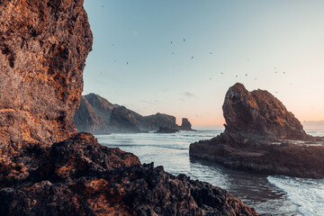 A picturesque view of rock formations in the ocean, bathed in the warm light of the setting sun.
