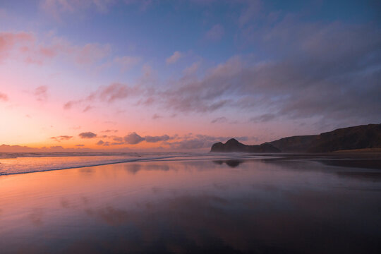 A stunning view of Bethells Beach, captured at sunset, with vibrant tones of pink, violet, and orange filling the sky.