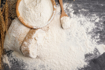 Flour in a sack and wheat flour in a wooden bowl There are ears of wheat on the table on, black background - Top view