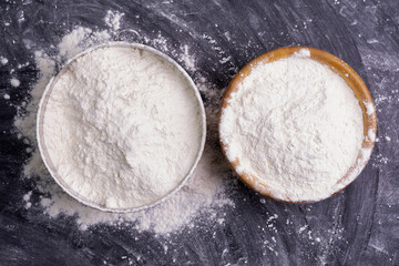 Flour in a bowl and wheat flour on table, black background In a rustic kitchen, top view