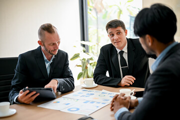 Colleagues meeting in the boardroom, sit at a table together, sharing ideas and discussing