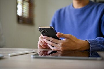 Cropped image of an Asian man using his smartphone at his desk. text, chat, message