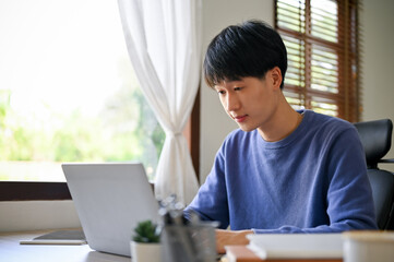 Smart young Asian male office worker focusing on his project on laptop, working in the office.