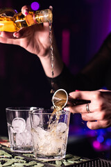 The bartender pours whiskey into a glass with ice. Mixing alcohol cocktail in nightclub, pub, restaurant