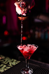 The bartender's hand pours alcohol into a glass with a long stem. Mixing alcohol cocktail in nightclub, pub, restaurant