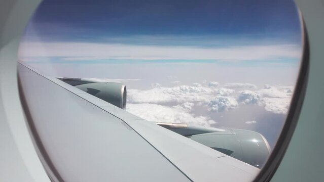 Large plane fly over flufy clouds on sunny day. View from passenger window to wing and two engines