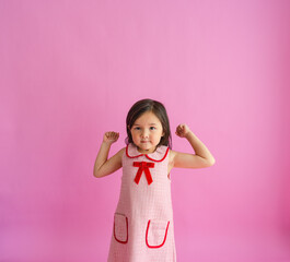 Cute elementary girl flexing muscles in front go pink backdrop