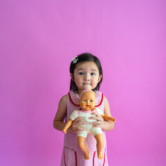 Cute little asian girl holding baby doll and smiling