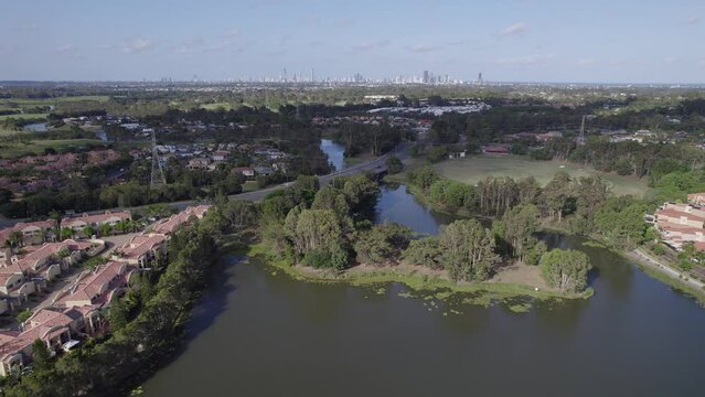 Mudgeeraba Creek Surrounded By Houses And Buildings In The Town Of Robina In Queensland, Australia. Coastal Skyline In Distance. aerial pullback