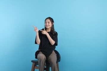 A young woman wearing black t-shirt, pointing with her fingers to empty space, gesture with hands on blue background