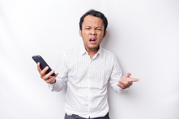 An angry young Asian man looks disgruntled wearing a white shirt irritated face expressions holding...