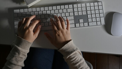 Top view of a female office worker working at her computer desk, typing on keyboard