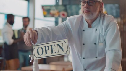 Mature chef turn open closed sign on glass door in cafe. Realtime