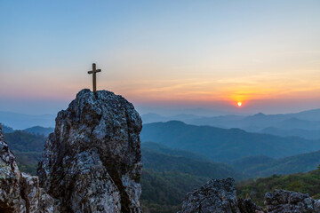 Silhouettes of crucifix symbol on top rock mountain with colorful sunset view background