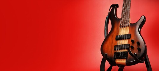  close up on 5 strings bass guitar at stand with natural finish, isolated on red with clipping...