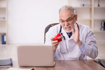 Old male cardiologist holding heart model