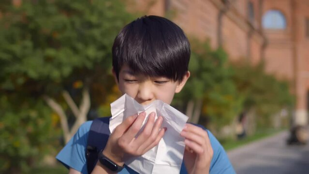 Asian sick schoolboy sneeze in tissue outdoors. Realtime