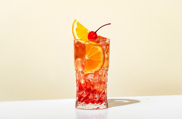Sex on the beach - popular alcoholic cocktail drink with vodka, peach liqueur, orange and cranberry juice, lemon and ice, garnished with cocktail cherry. Light beige background, hard light