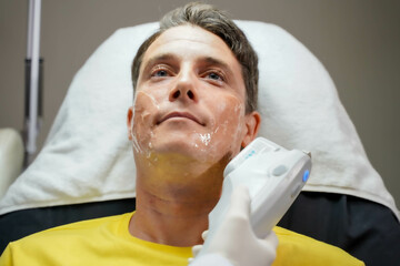 Closeup a male customer having color light therapy to stimulate facial skin by professional cosmetologist wellbeing.