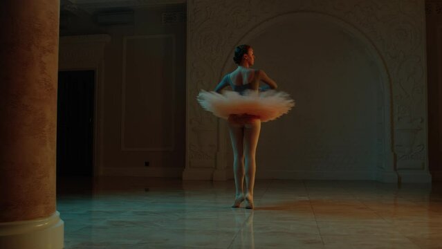 Cinematic shot of adult ballerina in tutu and pointes on choreography rehearsal in theater lobby. Female ballet dancer practices elegant movements before theatrical performance. Classical ballet art.
