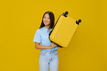 Asian woman traveling with yellow suitcase and tickets with passport in hand, tourist traveling by plane and train with luggage on yellow background in blue T-shirt and jeans