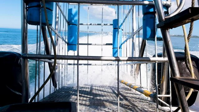 Shark cage diving boat speeds out to sea, backwards view of cage between engines