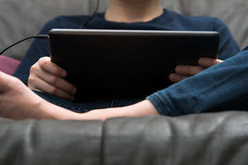 Digital tablet computer in male hands, from below view closeup. Guy sitting on sofa play videogame on handheld gadget.