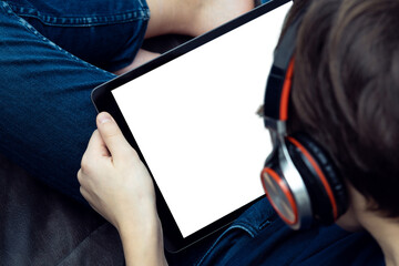 Digital tablet computer with blank white screen in male hands, from above view closeup. Young guy in headphones.