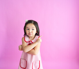 Pretty little girl crosses her arms while pointing off to the side and smiling. 
