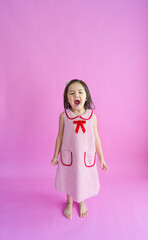 Pretty little girl standing in front of pink backdrop and shouting loud.
