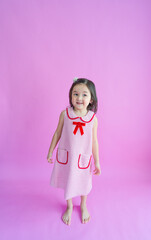 Pretty little girl standing in front of pink backdrop and smiling.