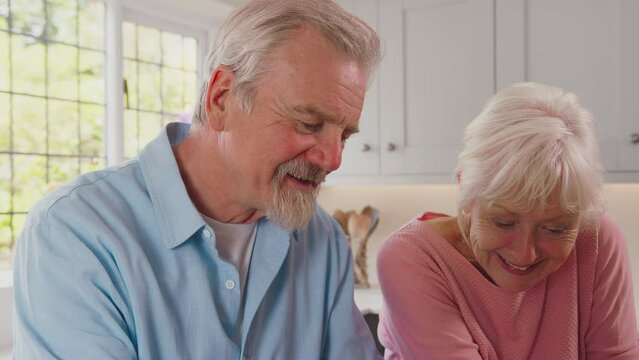 Smiling retired senior couple at home in kitchen signing legal or financial document together - shot in slow motion