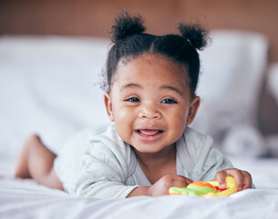 Happy, smile and portrait of a baby on a bed playing with a toy while relaxing in her nursery. Happiness, excited and girl infant or newborn laying in her bedroom while being playful in her house.