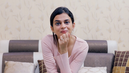 Medium shot of a beautiful young female talking while looking towards the camera. Point of view shot of a pretty Indian girl laughing while doing an online video call with her friend - technology c... - obrazy, fototapety, plakaty