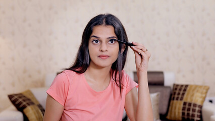 Medium shot of young Indian girl applying mascara on her eyelashes - makeup concept. Beautiful...