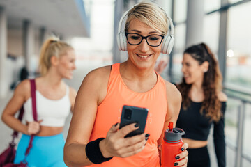 Happy middle adult woman looks at her phone in the gym