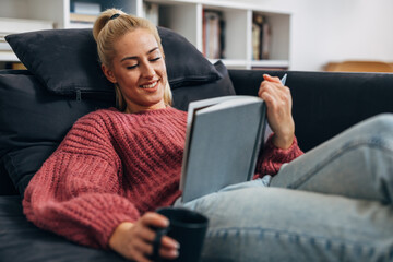 A blond Caucasian woman relaxes relaxes on the sofa with a book