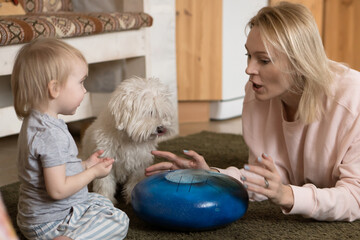 Mother and child playing music using hand pan glucophone drum with lap dog at home