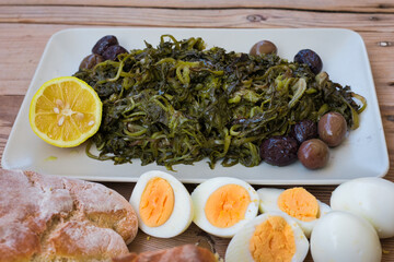 salad with boiled wild greens, dandelion, lemons and extra virgin olive oil, on a wooden table.  Horta or Wild Greens. Greek Cuisine.