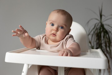 chubby baby in a white bodysuit sits in a white high chair for feeding