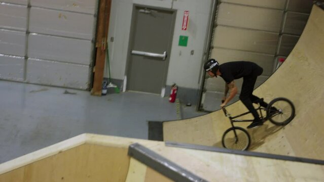 BMX rider catches air and does no hander over indoor box jump at indoor skatepark