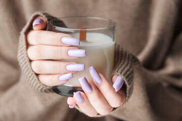 The hands of a young girl with a beautiful light purple manicure hold a candle