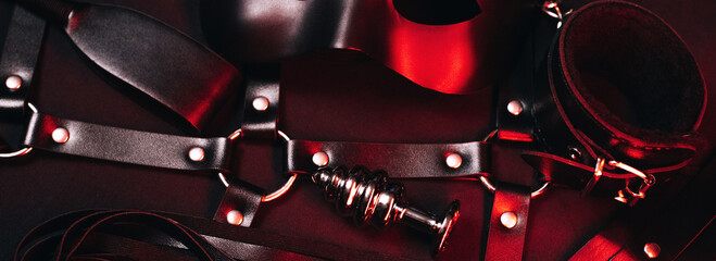 Female set of sex toys from a sex shop for BDSM sex with submission and domination. Mask, leather belt, choker, handcuffs, whip and anal plug. Panoramic wide horizontal photo for banner head cover - obrazy, fototapety, plakaty