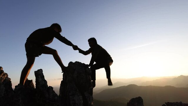Silhouette of two tourists lends helping hand climb cliffs mountains helping hand. teamwork helping hand business travel silhouette concept.  teamwork people climbers climb top overcoming hardships.
