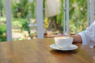 Closeup image of a hand holding coffee cup on wooden table in cafe