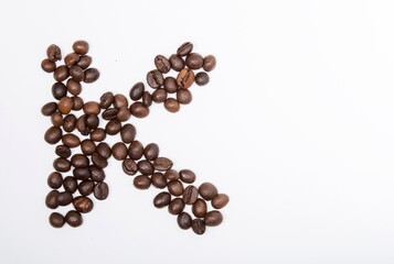 K is a capital letter of the English alphabet made up of natural roasted coffee beans that lie on a white background.